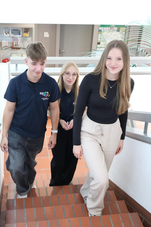 Drei jugendliche Auszubildende laufen eine Treppe hoch, sie haben freundliche Gesichter.